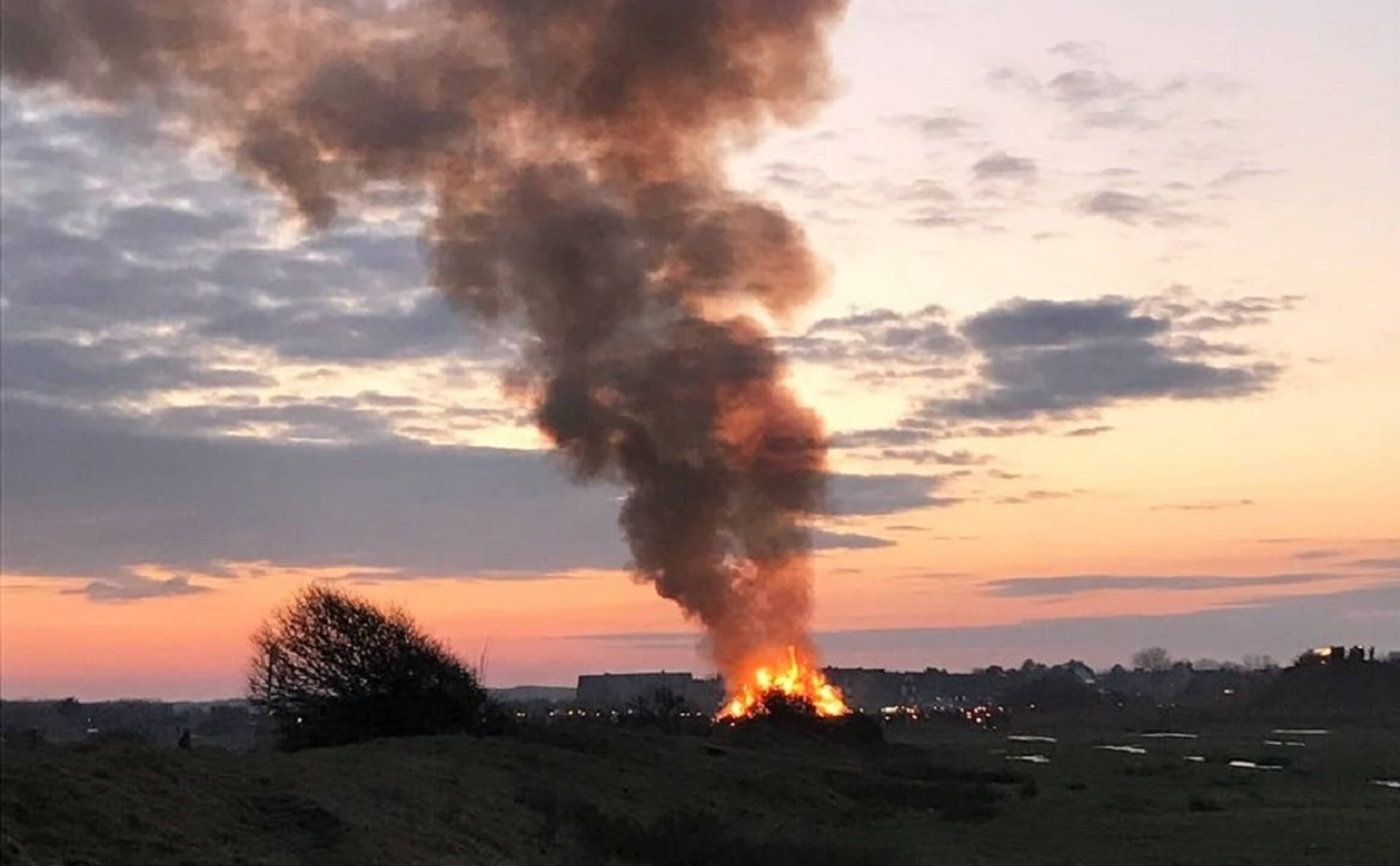 Biike Brennen auf Sylt | Severin*s Landhaus Morsum Kliff Sonnenuntergang über Sylt mit einem großen Osterfeuer, das Rauch in den Himmel aufsteigen lässt.