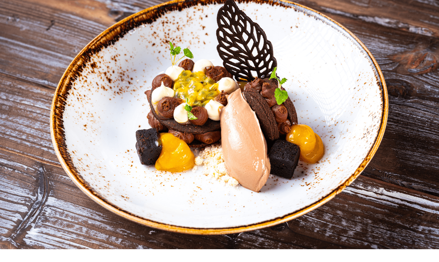 Elegantes Dessert mit Schokoladenmousse, Passionsfrucht und Schokoblatt, kunstvoll auf einem weißen Teller angerichtet.