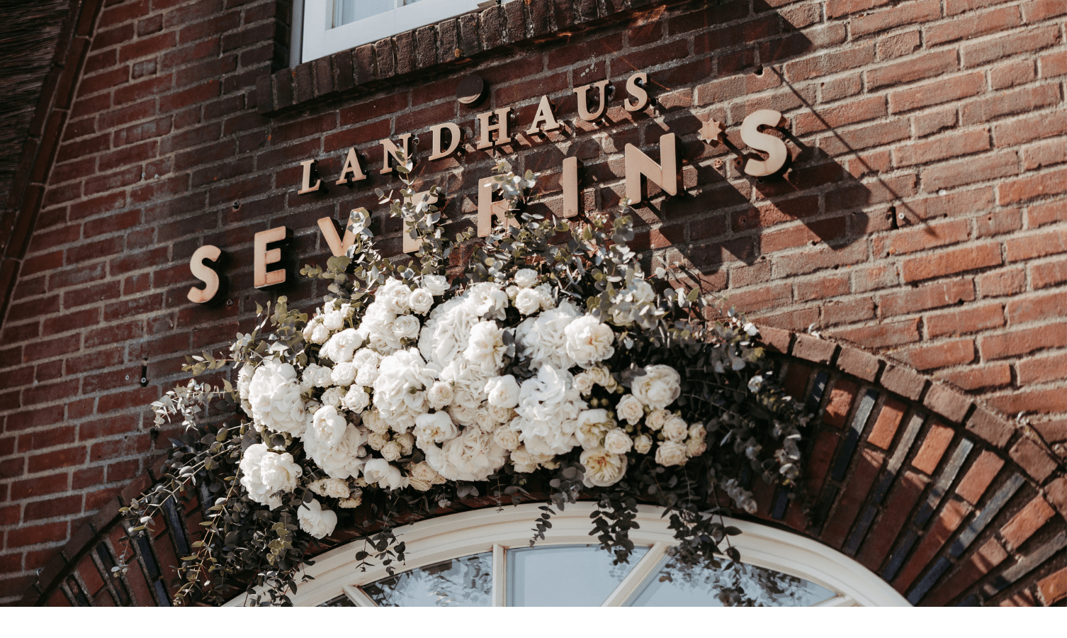 Blumendekoration Eingang – Landhaus Severin*s Backsteinfassade des Landhaus Severin*s mit weißen Blumen dekoriert.