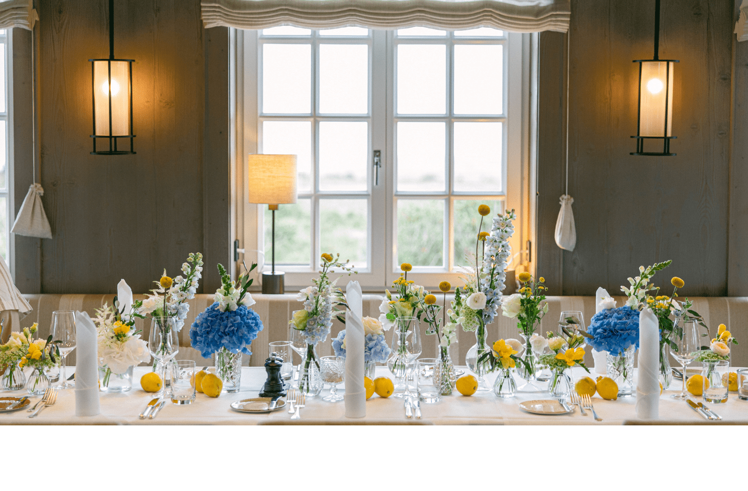 Eleganter, gedeckter Tisch mit blauen und gelben Blumenarrangements vor einem großen Fenster im Landhaus Severin*s Morsum Kliff.