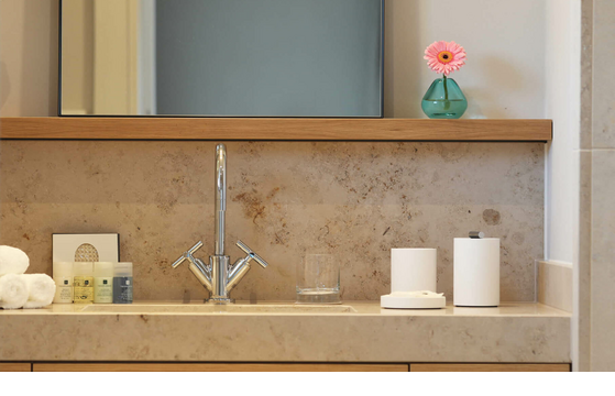 Modernes Badezimmer mit Waschtisch, Spiegel, Pflegeprodukten und rosa Blume in Vase im Hotel Landhaus Severin*s Morsum Kliff.