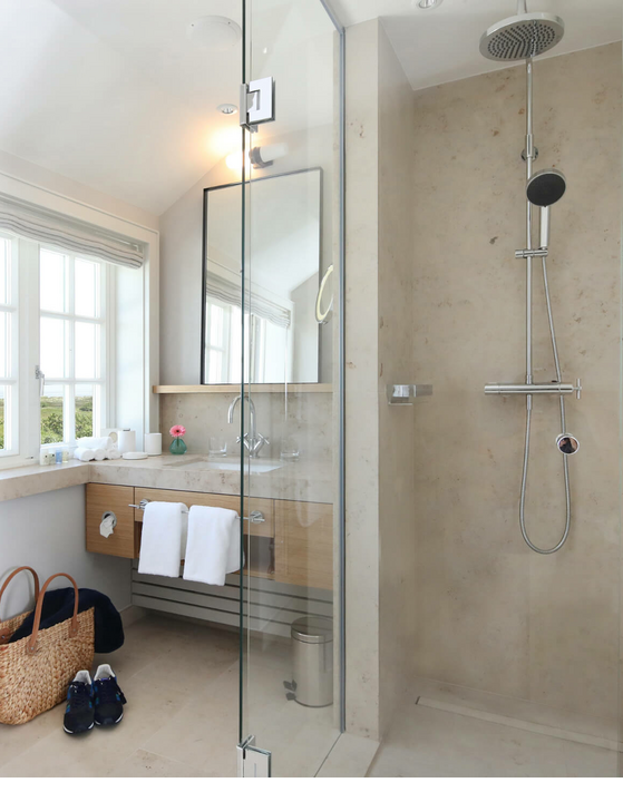 Modernes Badezimmer mit großer Dusche, Fenster mit Ausblick auf grüne Landschaft, Waschtisch mit Spiegel und Handtüchern.