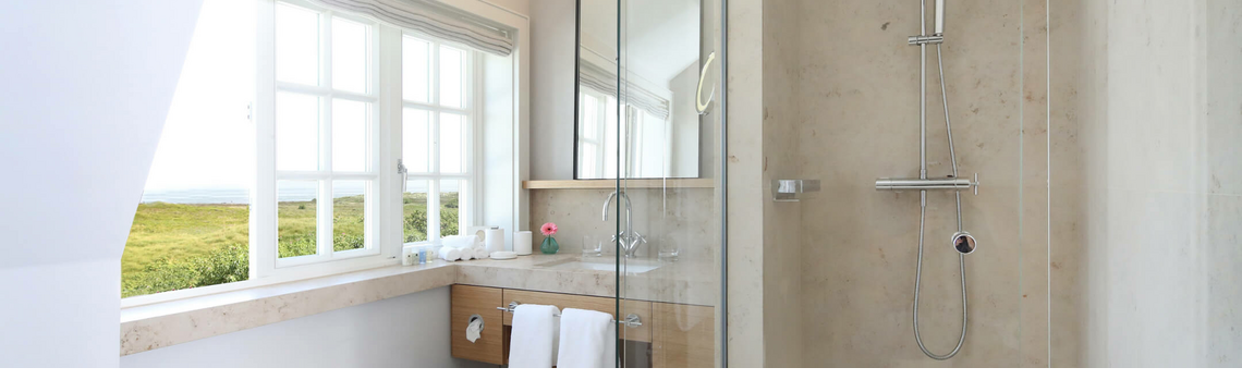 Modernes Badezimmer mit großer Dusche, Fenster mit Ausblick auf grüne Landschaft, Waschtisch mit Spiegel und Handtüchern.