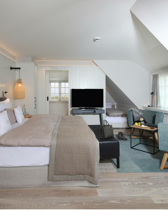 Helles, modernes Hotelzimmer mit Doppelbett, Sitzbereich, TV und Dachschräge im Landhaus Severin*s Morsum Kliff.