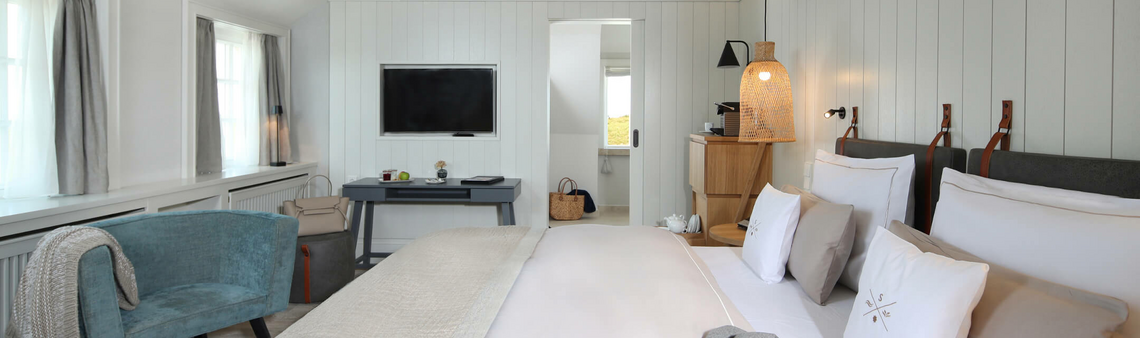 Helles Hotelzimmer mit Doppelbett, Sessel, Schreibtisch und TV. Moderne, gemütliche Einrichtung mit sanften Farben.