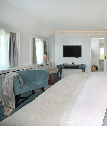 Helles Hotelzimmer mit Doppelbett, Sessel, Schreibtisch und TV. Moderne, gemütliche Einrichtung mit sanften Farben.