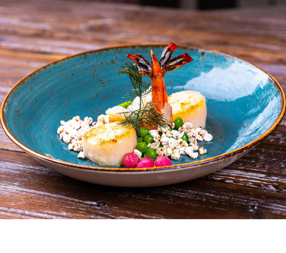 Gourmetgericht mit Jakobsmuscheln, Garnele, Erbsen und Popcorn auf blauem Teller, serviert im Landhaus Severin*s Morsum Kliff.