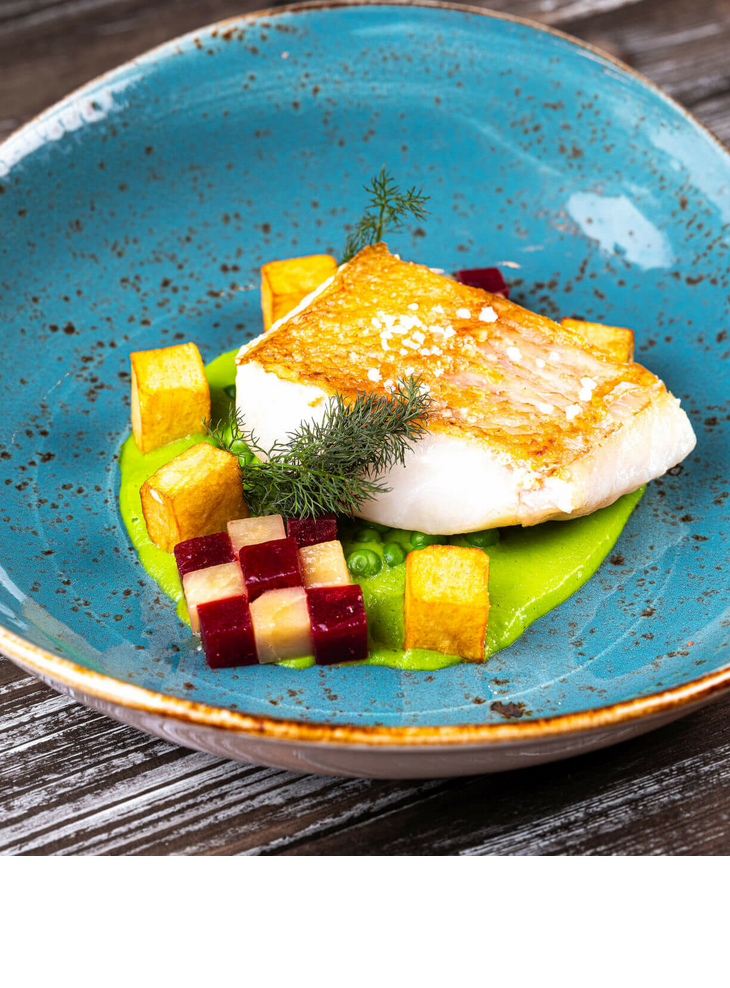 Gegrilltes Fischfilet auf Erbsenpüree mit bunten Gemüsewürfeln, serviert auf einem blauen Teller.