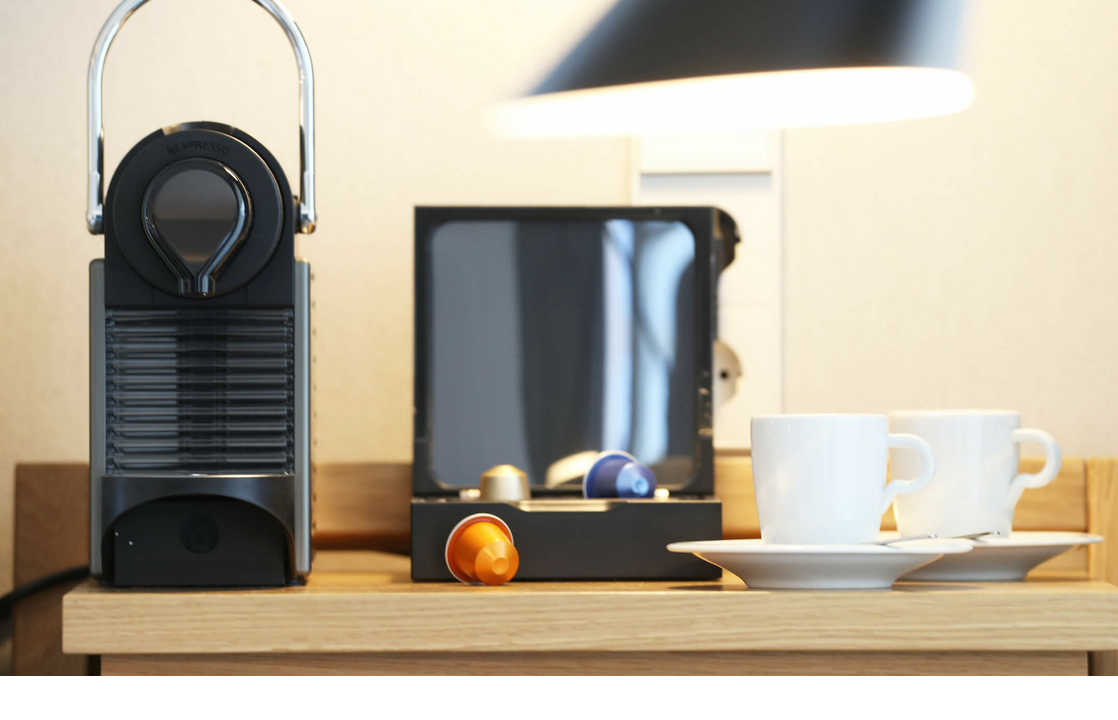 Kaffeemaschine mit Kapseln und zwei weißen Tassen auf Holzablage im Landhaus Severin*s Morsum Kliff Hotelzimmer.