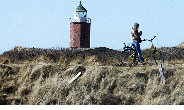 Radfahrerin vor dem Leuchtturm in Kampen auf Sylt Foto: ©Tom Kohler