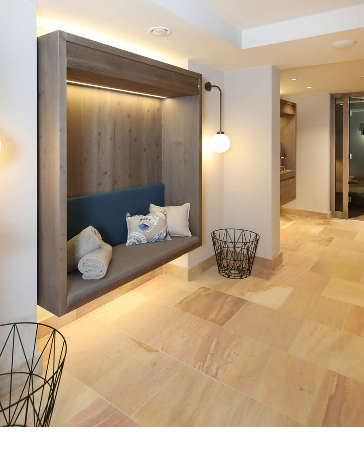 Wellnessbereich im Landhaus Severin*s Morsum Kliff auf Sylt Moderner Hotelflur mit Holzbank, Kissen, Decken, warmem Licht und Blick in einen gemütlichen Lounge-Bereich.