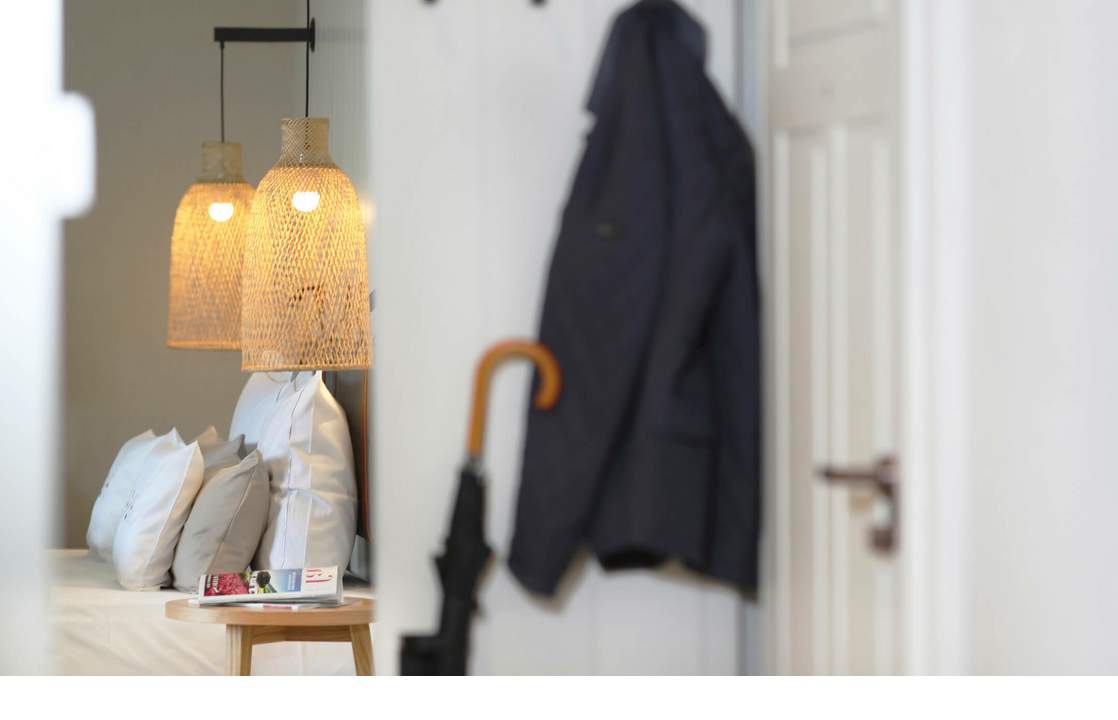 Gemütliches Hotelzimmer mit Bett, Rattanlampen und Garderobe mit Jacke und Regenschirm.