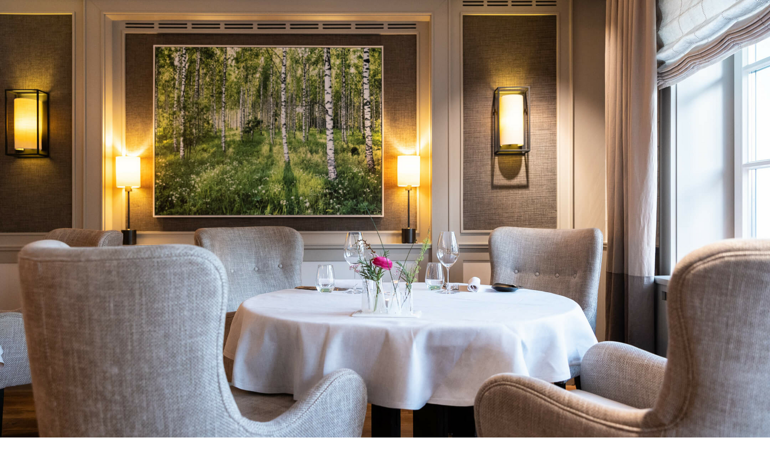 Fotokunst von Fotograf Andreas Wagner im Restaurant Tipken's by Nils Henkel | Severin*s Resort & Spa Sylt Elegantes Restaurant mit gedecktem Tisch, bequemen Sesseln und einem Gemälde von Birkenwald an der Wand.