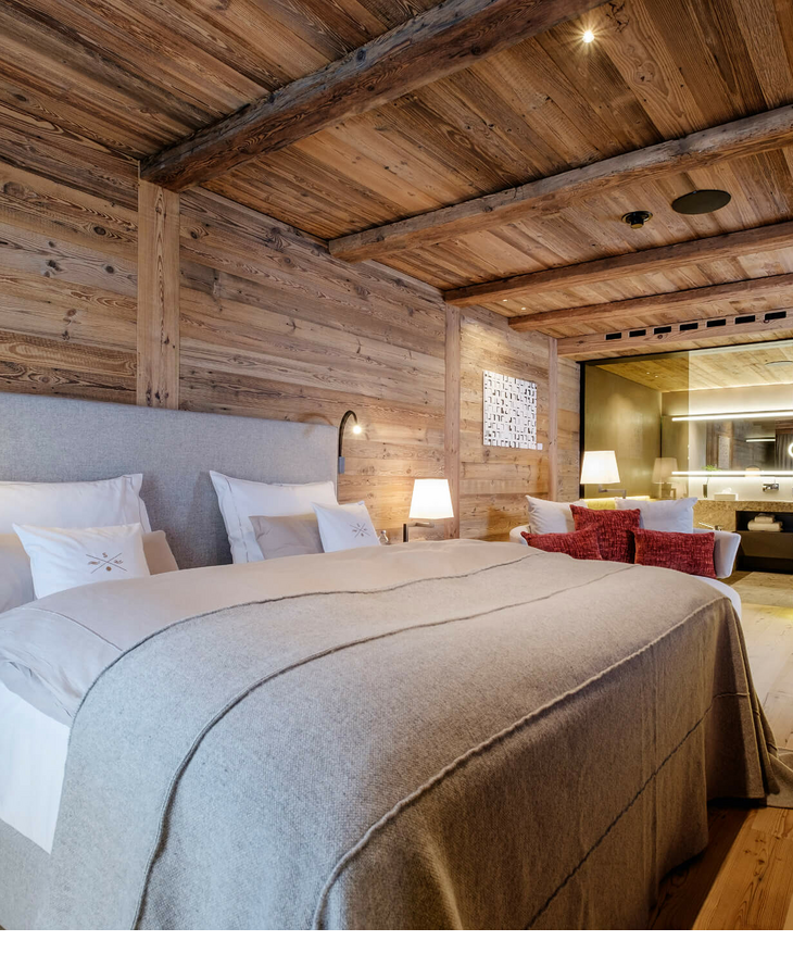 Gemütliches Hotelzimmer mit Holzwänden, großem Bett, moderner Beleuchtung und Blick ins luxuriöse Badezimmer.