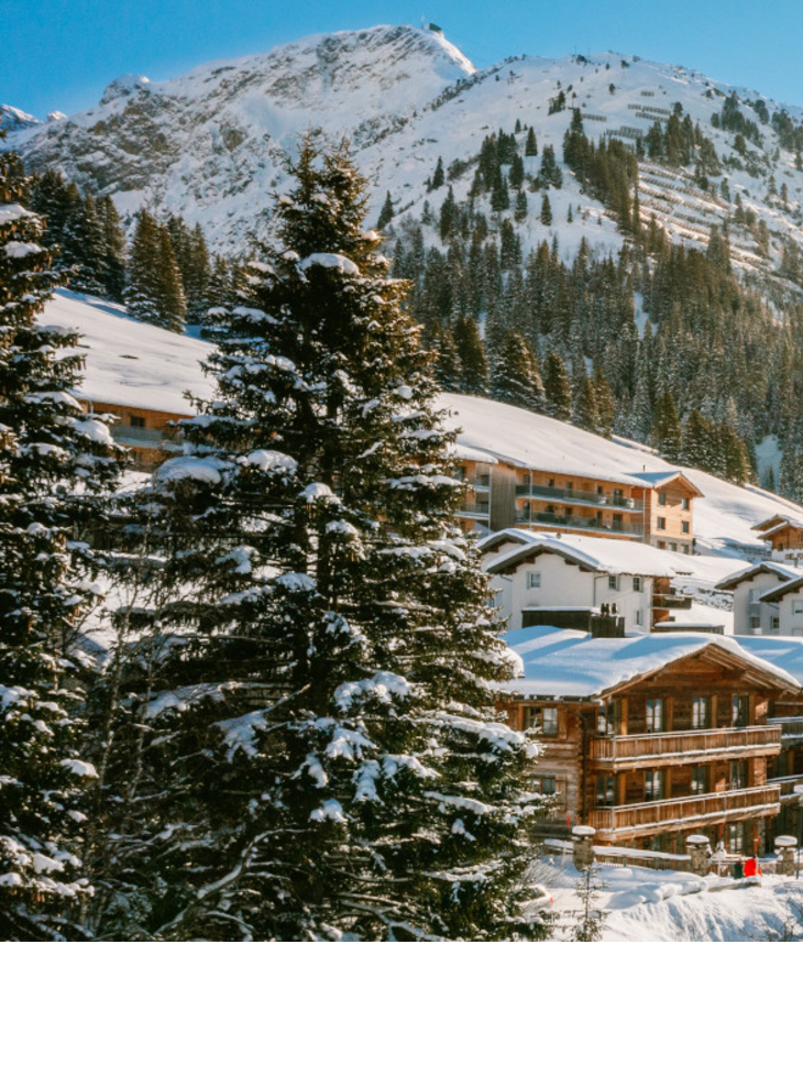Verschneite Alpenlandschaft mit Sonne über Hotel Severin*s in Lech, umgeben von Bergen und Bäumen.