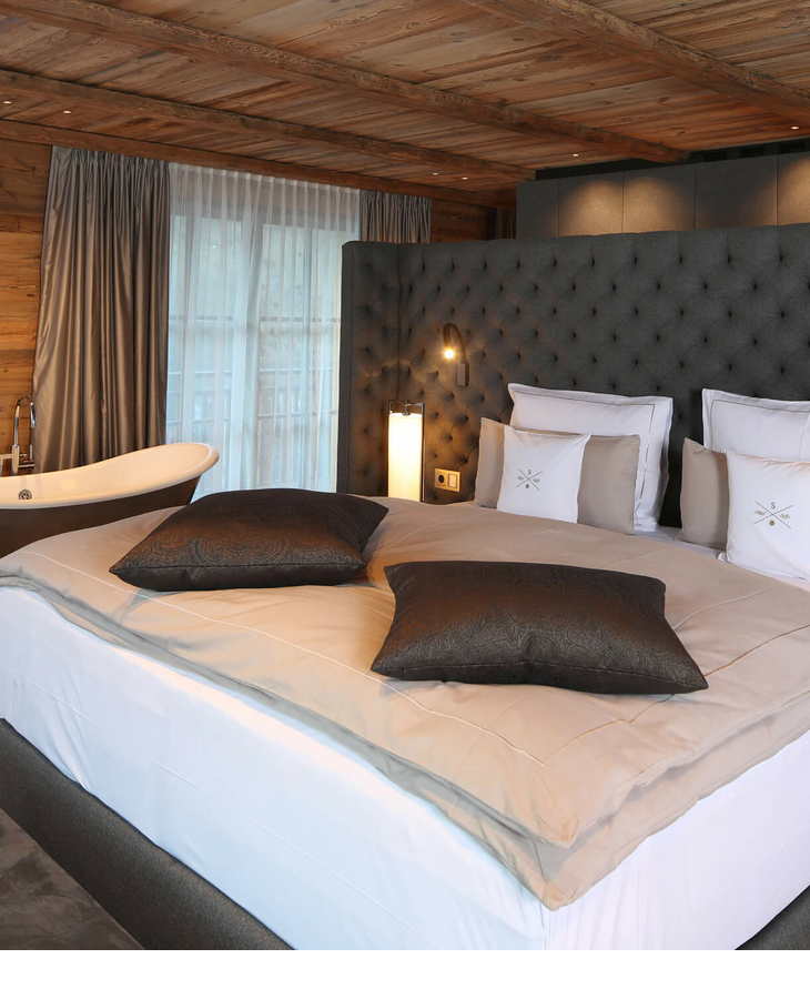 Luxuriöses Hotelzimmer mit großem Bett, freistehender Badewanne und eleganter Holzeinrichtung im Severin*s The Alpine Retreat.
