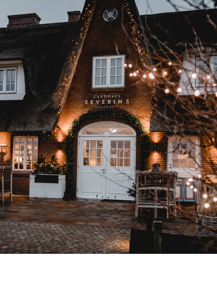 Reetgedecktes Hotel Landhaus Severin*s bei Dämmerung, mit Lichterketten beleuchtet, einladende Atmosphäre.