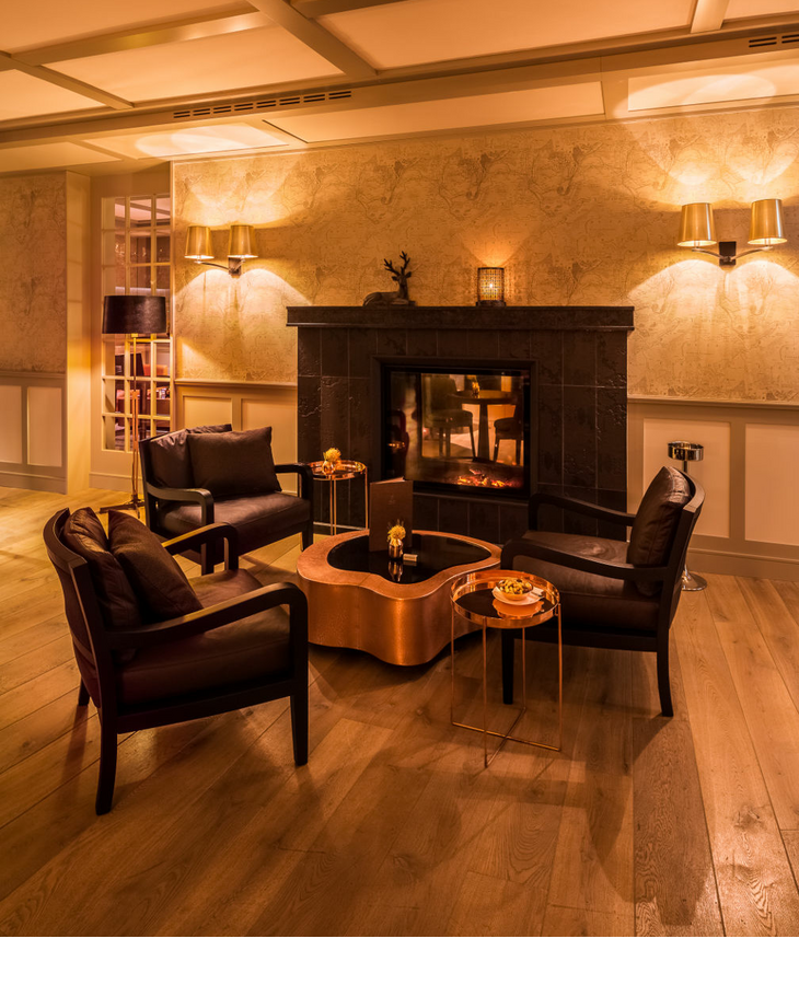 Gemütliche Sitzecke mit Kamin, vier Sesseln und Holztisch im Severin*s Resort & Spa auf Sylt, warm beleuchtet.