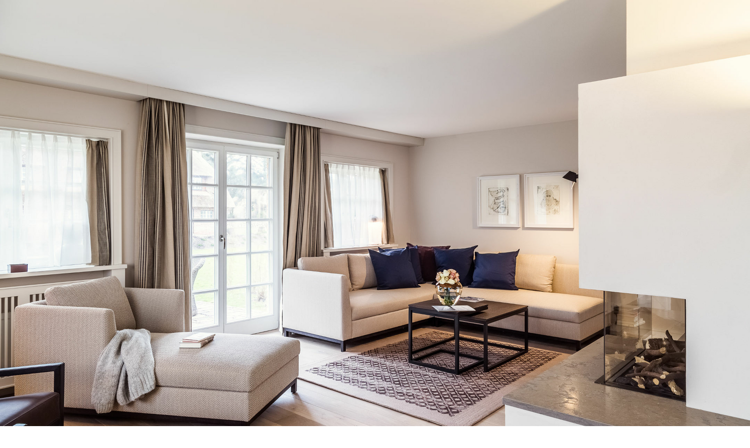 Helles Wohnzimmer mit beiger Couch, blauen Kissen, Kamin, Sessel und großem Fenster im Severin*s Resort & Spa, Sylt.