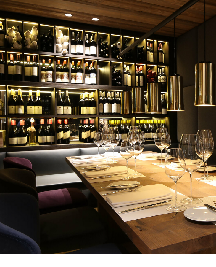 Elegantes Restaurant mit gedecktem Tisch, Weingläsern und beleuchteter Weinregalwand im Severin*s The Alpine Retreat.